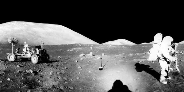 Apollo astronauts on the moon with the lunar rover in the background.